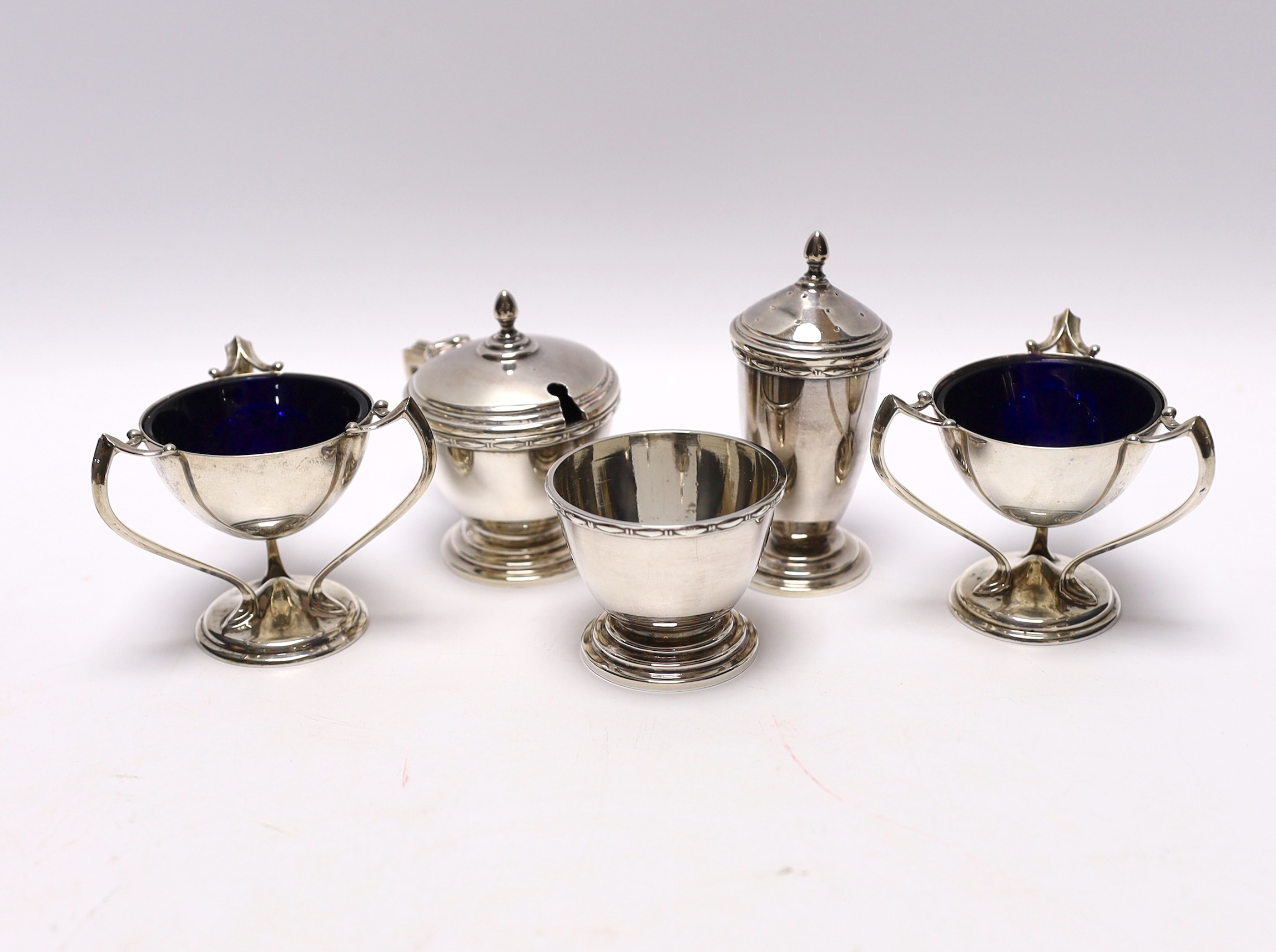 A pair of Edwardian Art Nouveau silver tri-handled salts, Richard Richardson, Sheffield, 1905, height 59mm, together with a later silver three piece condiment set, with two spoons (one plated).
